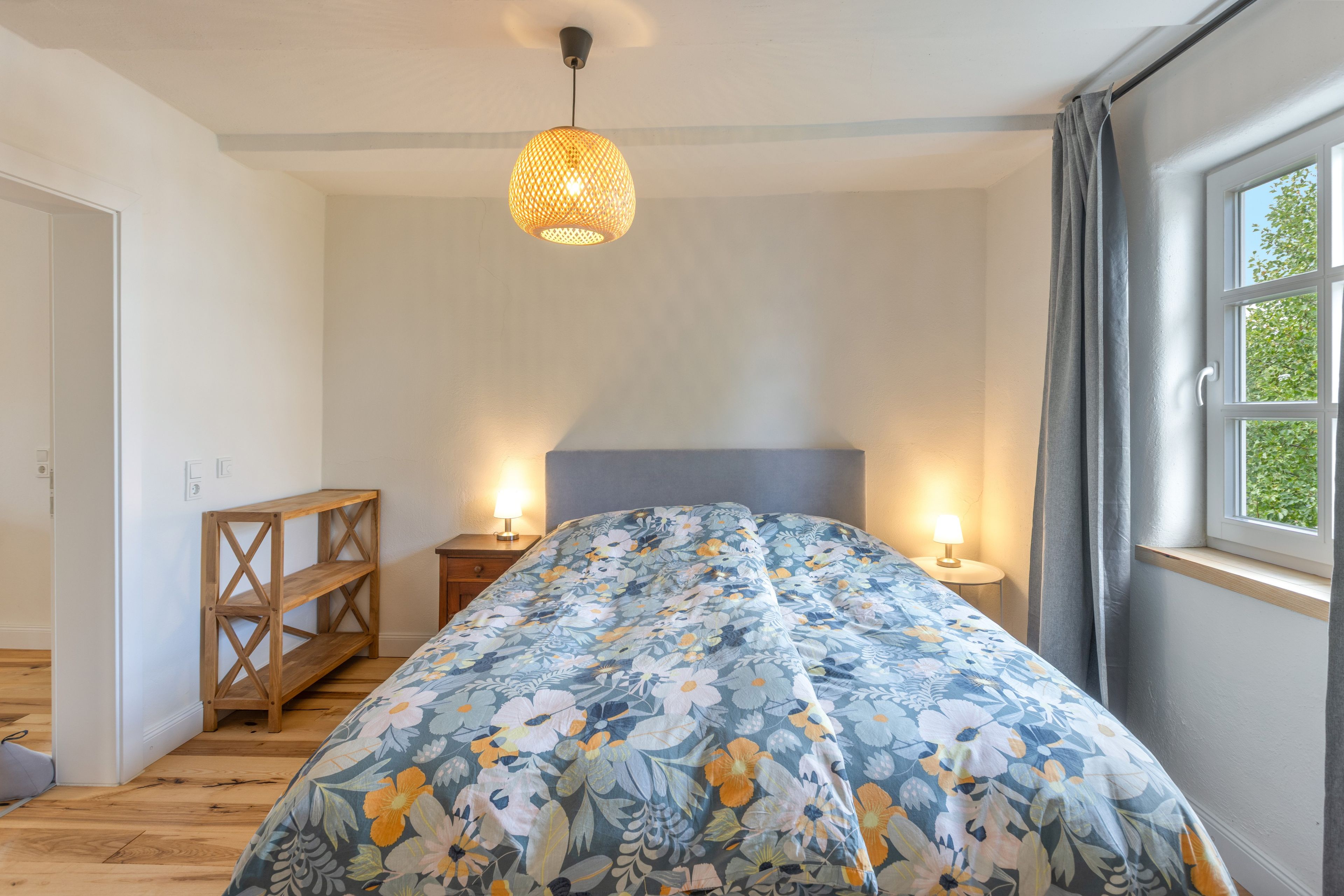 Ein Schlafzimmer mit einem Bett, Nachttischlampen, einem Holzregal und einem Fenster mit Vorhängen.