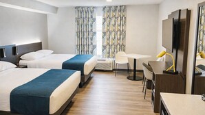 Une chambre d’hôtel avec deux lits, un bureau, une chaise, une télévision et des rideaux à motifs.