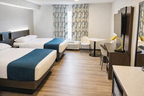 Hotelkamer met twee bedden, een bureau, een stoel, een televisie en gordijnen met een patroon.