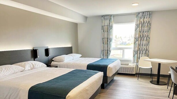 Une chambre d’hôtel avec deux lits, une petite table, des chaises et une fenêtre avec des rideaux.