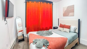 A modern bedroom with a bed, a bedside table, a mirror, and a TV mounted on the wall. - 20 Mins to Manhattan w/Full kitchen (Apt. 5) (West New York)