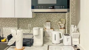 A modern kitchen with white cabinets, a microwave, a coffee maker, a kettle, a toaster, and a knife block. - 20 Mins to Manhattan w/Full kitchen (Apt. 5) (West New York)