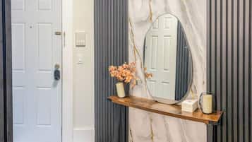 A hallway with a white door, a mirror on a wooden shelf, and a marble wall.