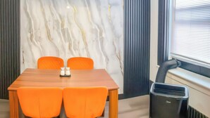 A conference room with a wooden table, four orange chairs, a marble wall, a black trash bin, and a window with blinds. - 20 Mins to Manhattan w/Full kitchen (Apt. 5) (West New York)