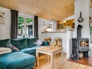 A cozy living room with a sofa, a table with bottles, a kitchen area with wooden cabinets, and a wood-burning stove. - "Söffren" - 450m to the fjord by Interhome (Øster Assels)