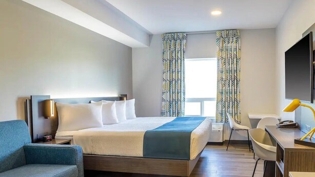 Une chambre d’hôtel moderne équipée d’un lit, d’un bureau, d’une chaise et d’un téléviseur.