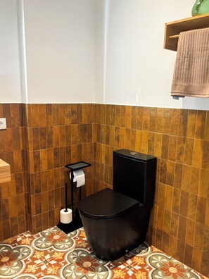 Une salle de bain avec des toilettes noires, un porte-rouleau de papier toilette et un carrelage décoré.