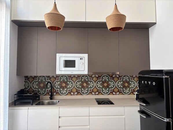 A modern kitchen with a microwave, two hanging light fixtures, a sink, and a refrigerator. - Apartment in El Cabanyal, 5 minutes from the beach (València)
