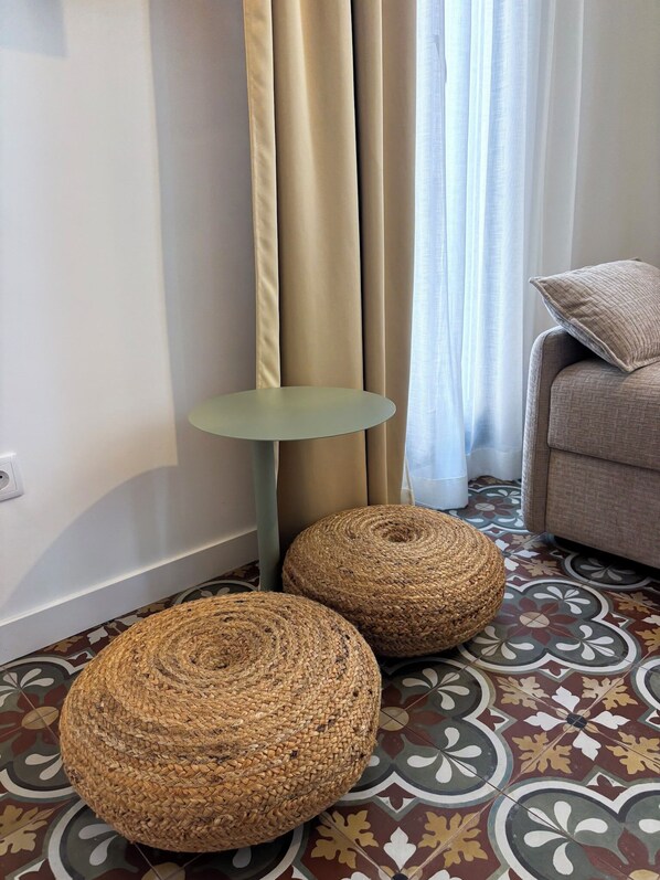 A room with a patterned floor, a small round table, two woven ottomans, and a sofa with a cushion. - Apartment in El Cabanyal, 5 minutes from the beach (València)