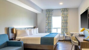 A modern hotel room with a bed, a desk, a chair, and a TV. - King Room with Kitchen | Free Parking | Quick 0.5-Mile Drive to Cedar Point (Hornepayne)