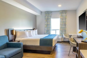 A modern hotel room with a bed, a desk, a chair, and a TV. - King Room with Kitchen | Free Parking | Quick 0.5-Mile Drive to Cedar Point (Hornepayne)