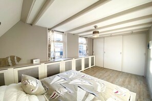 A bedroom with a sloped ceiling, a bed with a patterned bedspread, a window with curtains, and a wardrobe. - SE06 Holiday home Serooskerke (Serooskerke)