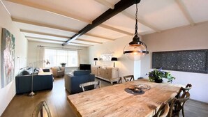 Un'ampia sala da pranzo con tavolo e sedie in legno, un lampadario e vista sul soggiorno.