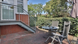 Een terras met een tafel en stoelen, een metalen trap en een haag.