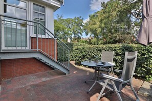 A patio area with a table and chairs, a metal staircase, and a hedge. - Vrbo Property (Langeoog)