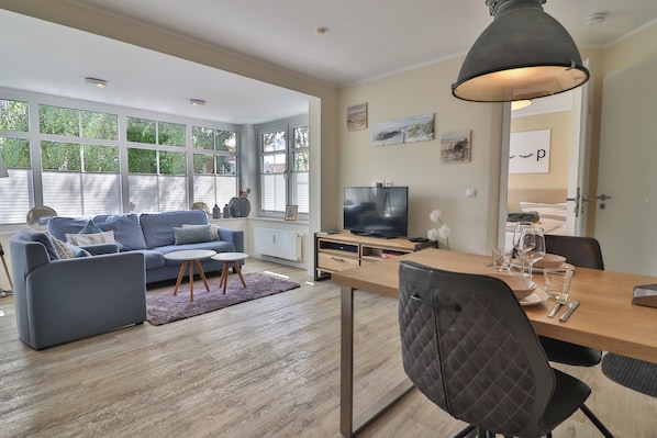 A modern living room with a sofa, coffee table, and dining table. - Vrbo Property (Langeoog)
