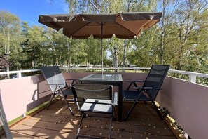 Een terras met een tafel met glazen blad, twee stoelen en een bruine parasol.