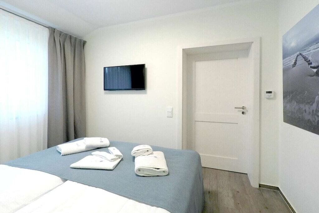 Et hotelværelse med en seng, et vægmonteret fladskærms-tv, en dør og et billede på væggen.