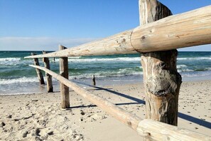 Een houten constructie op een zanderig strand, met de oceaan op de achtergrond.