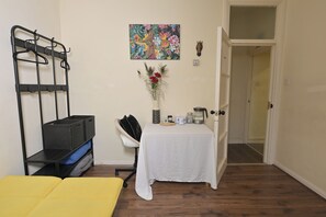 A room with a bed, a small table with items, a chair, a coat rack, and a door leading to another room. - London Cozy Apartment Retreat (London)