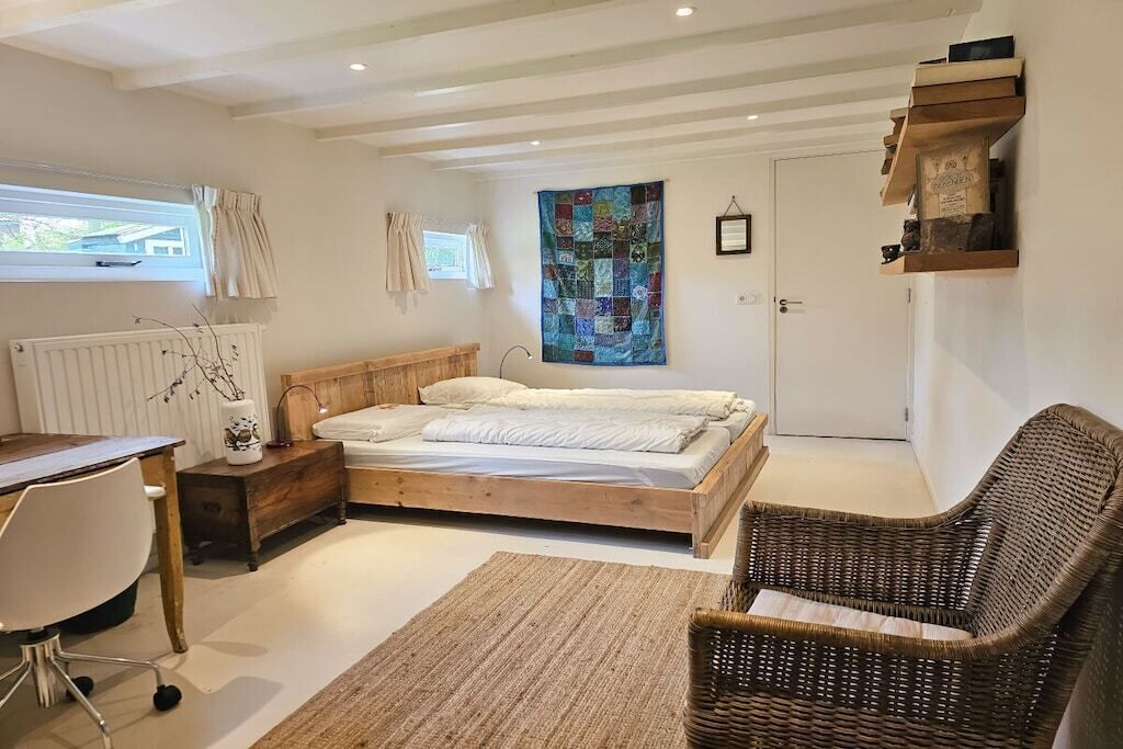 A bedroom with a wooden bed, a desk, a chair, a radiator, and a window with curtains.