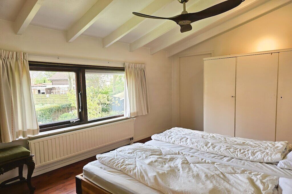 Ein Schlafzimmer mit einem Bett, einem Fenster mit Vorhängen, einem Heizkörper und einem Deckenventilator.
