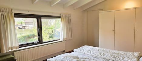 Een slaapkamer met een bed, een raam met gordijnen, een radiator en een plafondventilator.