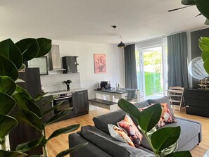 A modern kitchen with a dining area, a sofa with decorative pillows, and a large window with curtains. - Apartment 'Zwergenwald' with Garage incl. Charging Station, Terrace, Garden & Wi-Fi (Badenweiler)