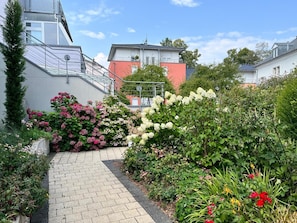 A paved pathway leading through a garden with various flowering plants and shrubs. - Apartment 'Zwergenwald' with Garage incl. Charging Station, Terrace, Garden & Wi-Fi (Badenweiler)