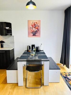A compact kitchen with a dining table, chairs, and a coffee machine. - Apartment 'Zwergenwald' with Garage incl. Charging Station, Terrace, Garden & Wi-Fi (Badenweiler)