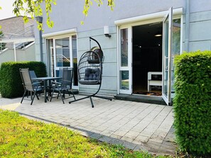 An outdoor patio area with a table and chairs, a hanging chair, and a door leading to the interior. - Apartment 'Zwergenwald' with Garage incl. Charging Station, Terrace, Garden & Wi-Fi (Badenweiler)