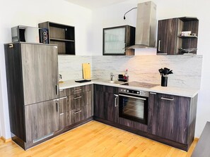 A modern kitchen with dark wood cabinets, a built-in oven, a microwave, and a stainless steel range hood. - Apartment 'Zwergenwald' with Garage incl. Charging Station, Terrace, Garden & Wi-Fi (Badenweiler)