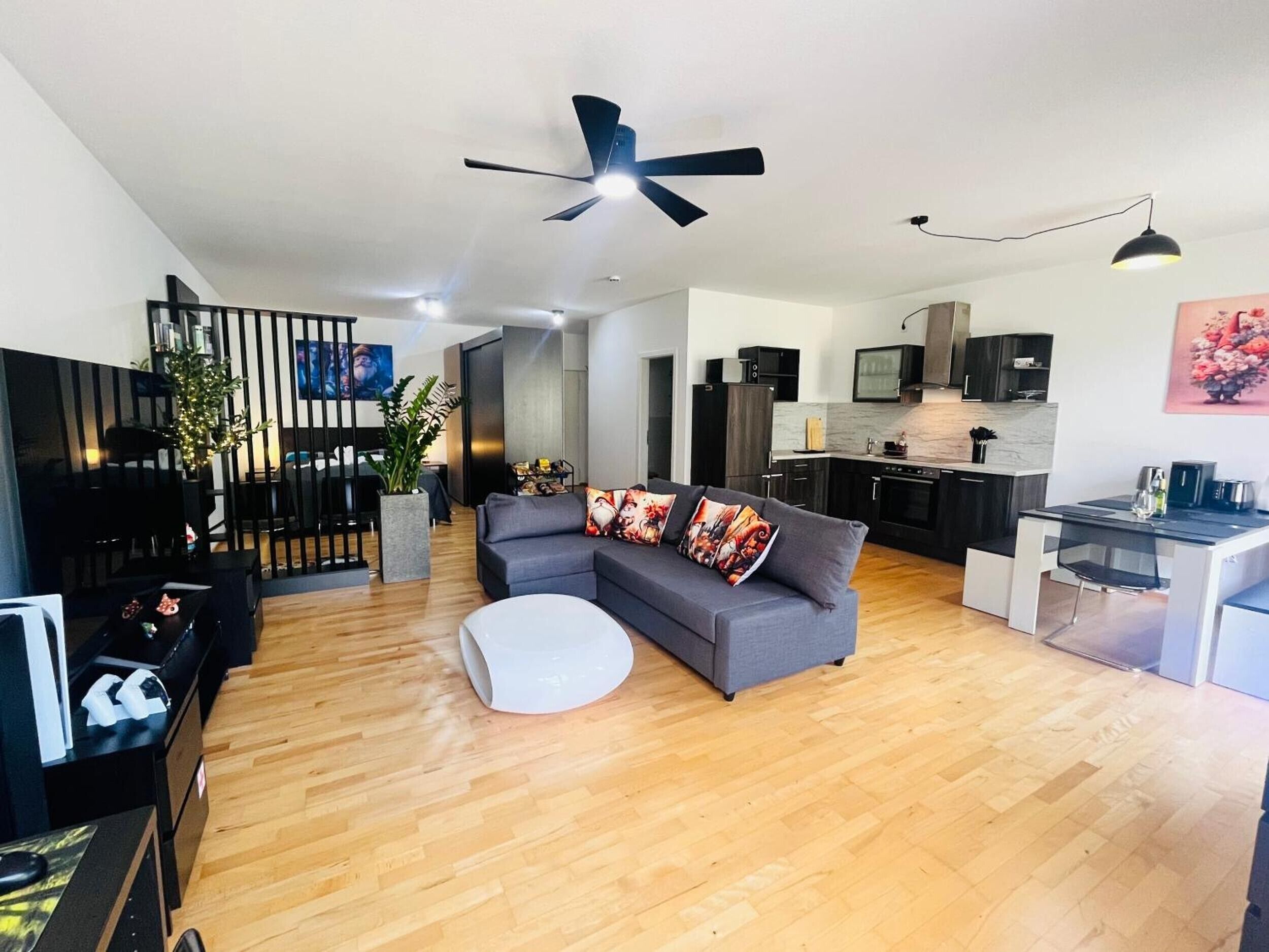Un salon moderne avec un canapé gris, un pouf blanc et un coin repas doté d’une table en verre.