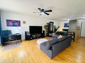 A modern living room with a grey sofa, a flat-screen TV, a ceiling fan, and a wooden floor. - Apartment 'Zwergenwald' with Garage incl. Charging Station, Terrace, Garden & Wi-Fi (Badenweiler)
