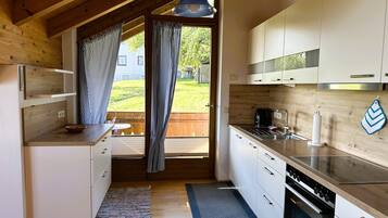 Eine moderne Küche mit Holzbalken, einem großen Fenster mit Vorhängen, einem eingebauten Backofen und weißen Schränken.