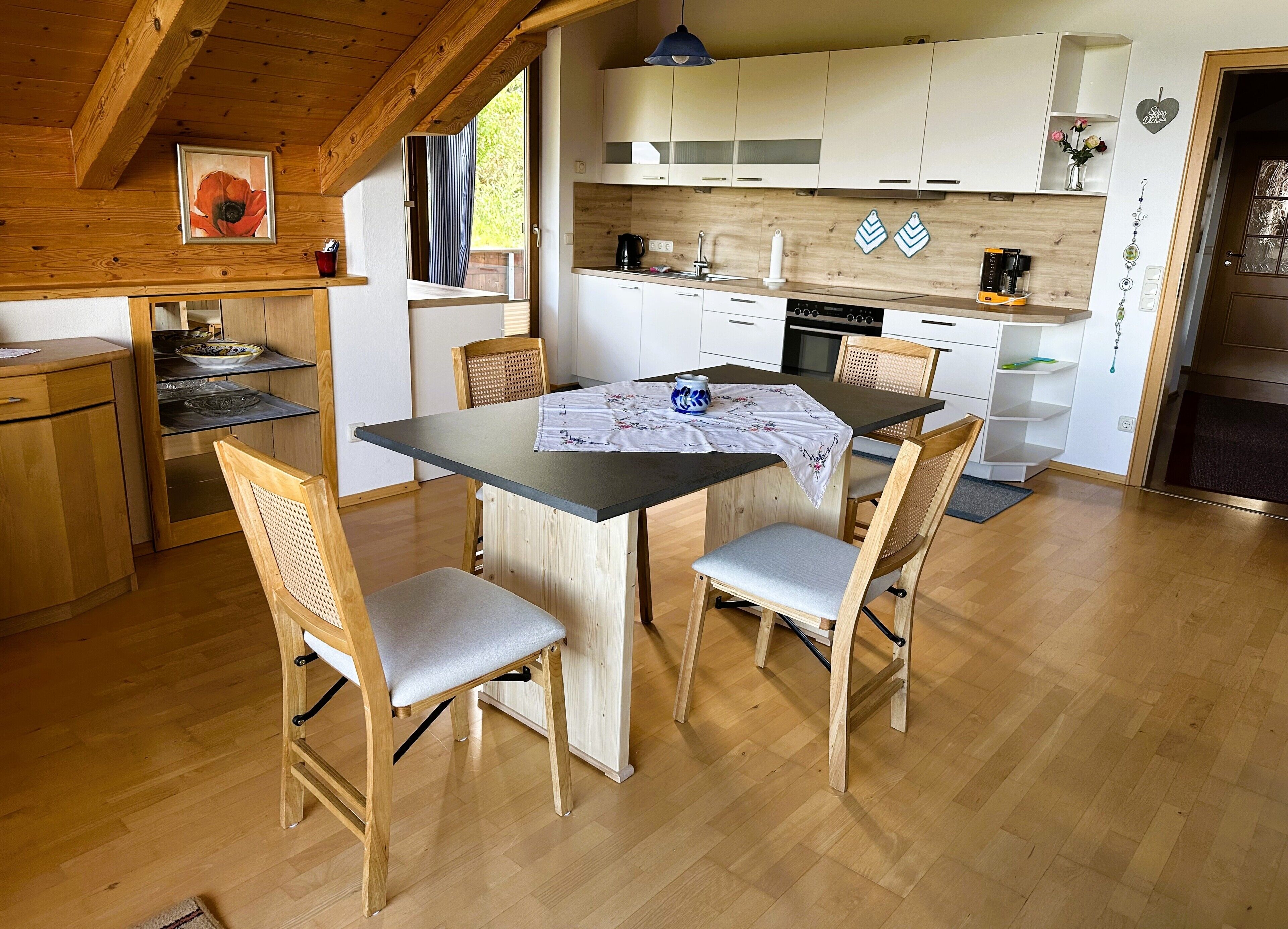 Eine moderne Küche mit Holzschränken, einem Esstisch mit Stühlen und Blick ins Freie.