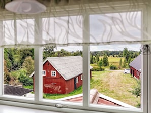Udsigt gennem et vindue af en rød lade og en græsmark med træer i baggrunden.