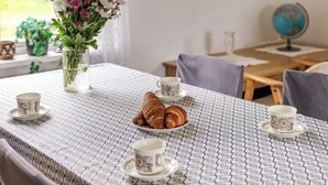 Een tafel met een tafelkleed met patroon, twee bekers, een bord met croissants en een vaas met bloemen.