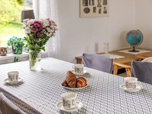 A table with a patterned tablecloth, two cups, a plate with croissants, and a vase with flowers. - Lantdrömmen by Interhome (Hyltebruk)