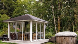 Een overdekt terras met een tafel, stoelen, een barbecue en een houten terras.