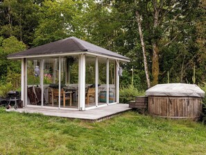 A covered outdoor seating area with a table and chairs, a grill, and a wooden deck. - Lantdrömmen by Interhome (Hyltebruk)