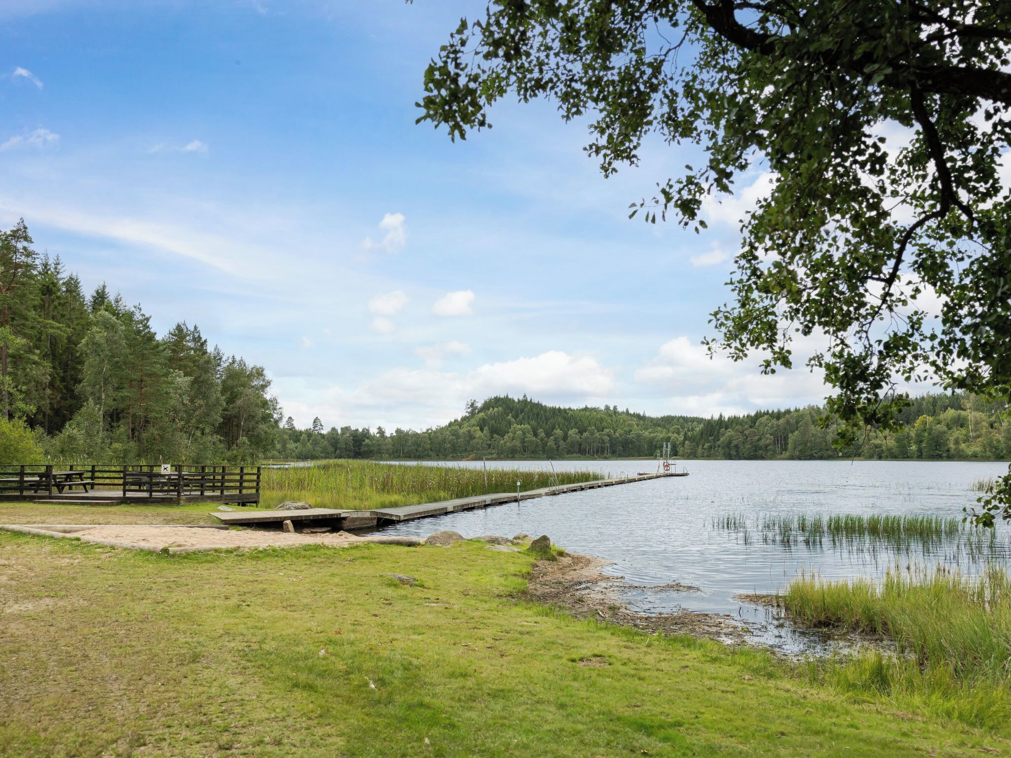 A lakeside park with a wooden dock, picnic tables, and a grassy area.