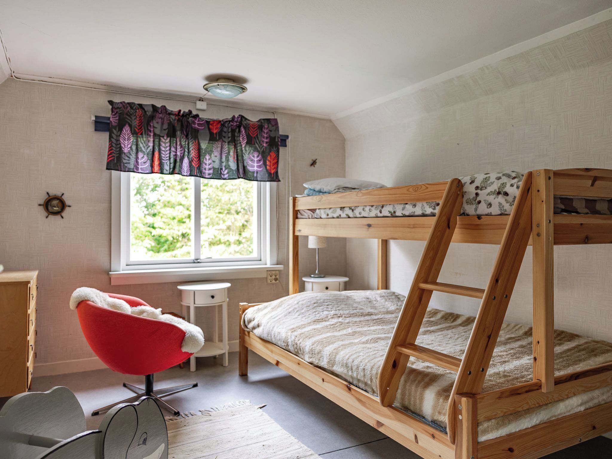A bunk bed room with a desk, chair, and a window with curtains.