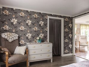 A bedroom with a floral wallpaper, a wooden chair with a cushion, a white dresser with drawers, and a grey curtain. - Lantdrömmen by Interhome (Hyltebruk)