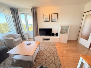 Ein modernes Wohnzimmer mit einem Flachbildfernseher, einer Couch, einem Couchtisch und einem gemusterten Teppich.