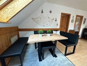 Zona pranzo con tavolo in legno, panche nere e due piante in vaso.