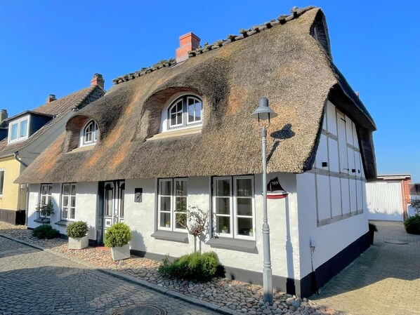 Un tipico cottage con tetto di paglia, esterno bianco, un piccolo portico e un lampione.