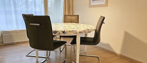 A dining area with a round table, four chairs, and a pendant light.