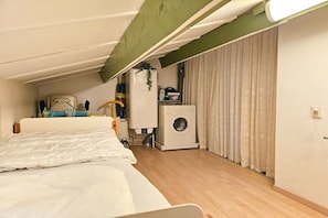 Ein kleines Zimmer mit einem Bett, einer Waschmaschine und einer kleinen Küchenzeile.