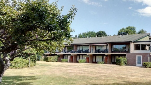 A two-story building with a flat roof, a covered outdoor seating area, and a grassy courtyard. - OK24 Holiday home with dog Oostkapelle (Oostkapelle)